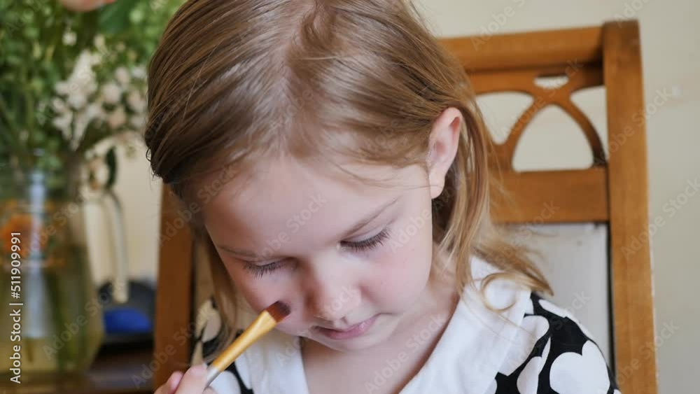 a cute preschooler girl ineptly uses her mother's cosmetics applies foundation on her face using a brush. a cute preschooler girl ineptly uses her mother's cosmetics applies foundation on her face using a brush.