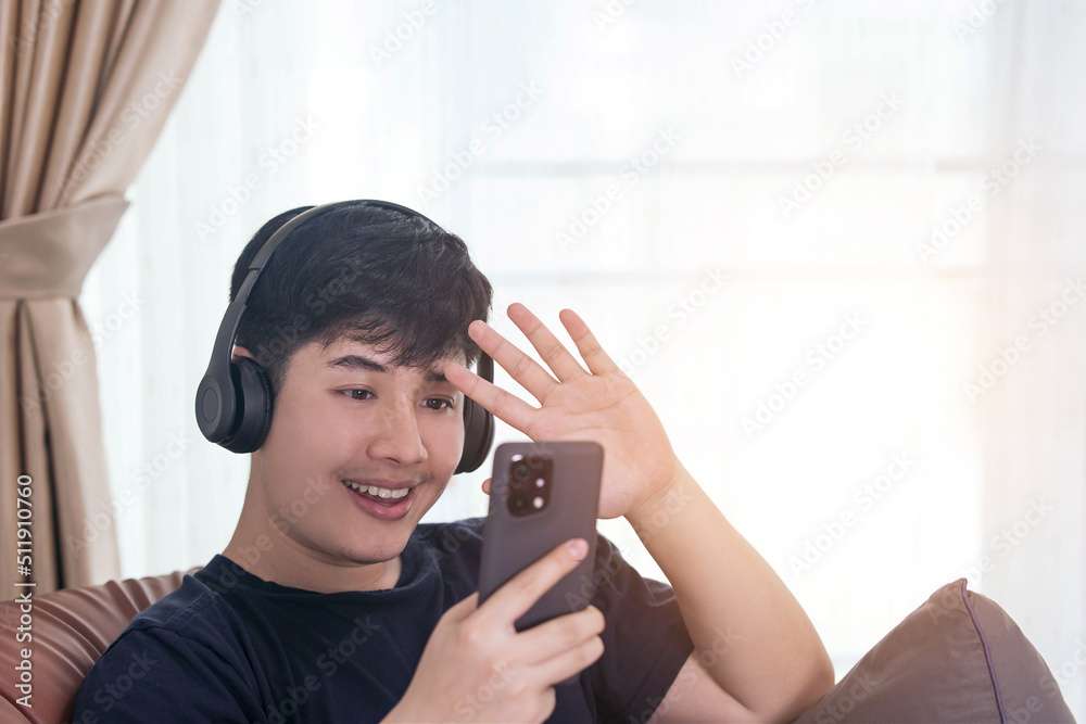 Handsome young man holding a smartphone while waving a video call on the sofa. Concept of online video chatting via 5G internet work with Social Network Application. Handsome young man holding a smartphone while waving a video call on the sofa. Concept of online video chatting via 5G internet work with Social Network Application.