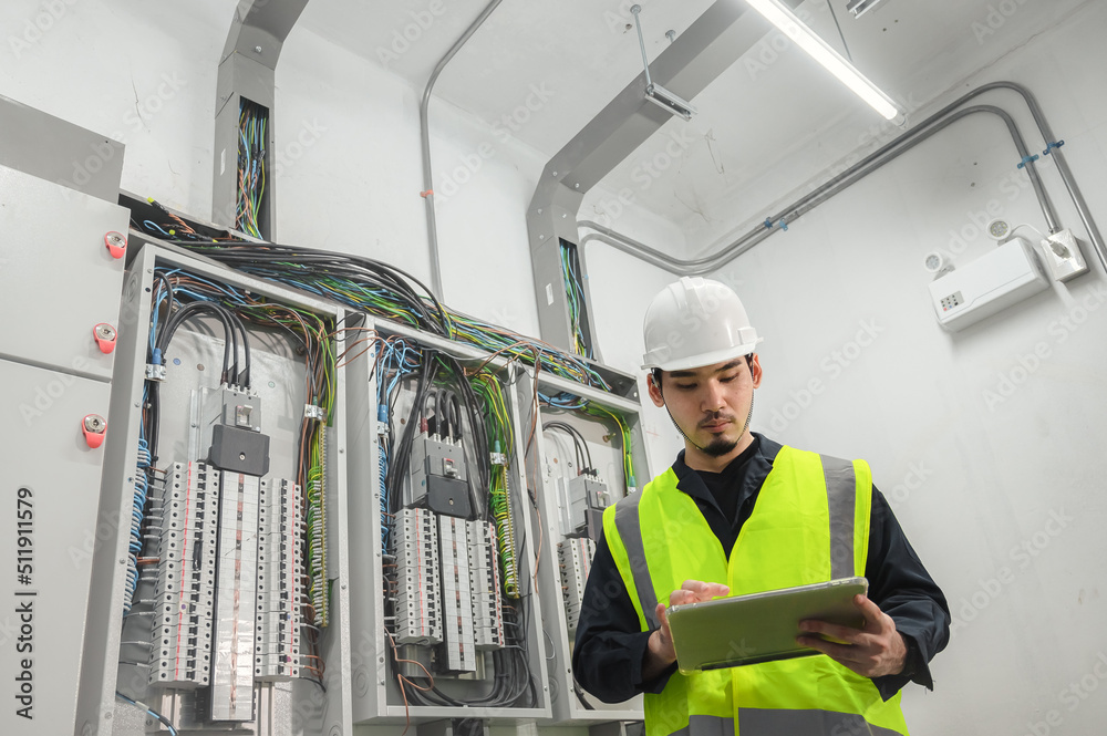 Electrical Engineer team working front control panel, An electrical engineer is installing and using a tablet to monitor the operation of an electrical control panel in a factory service room. Electrical Engineer team working front control panel, An electrical engineer is installing and using a tablet to monitor the operation of an electrical control panel in a factory service room.