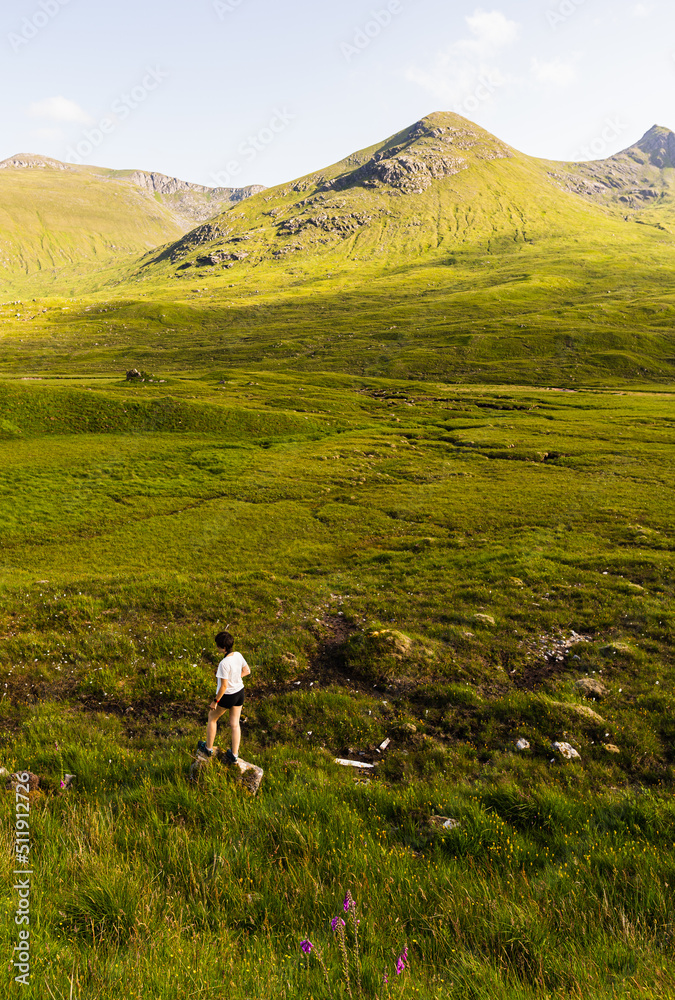 Young female walking alone around a big meadow on a summer day in the Highlands, Scotland