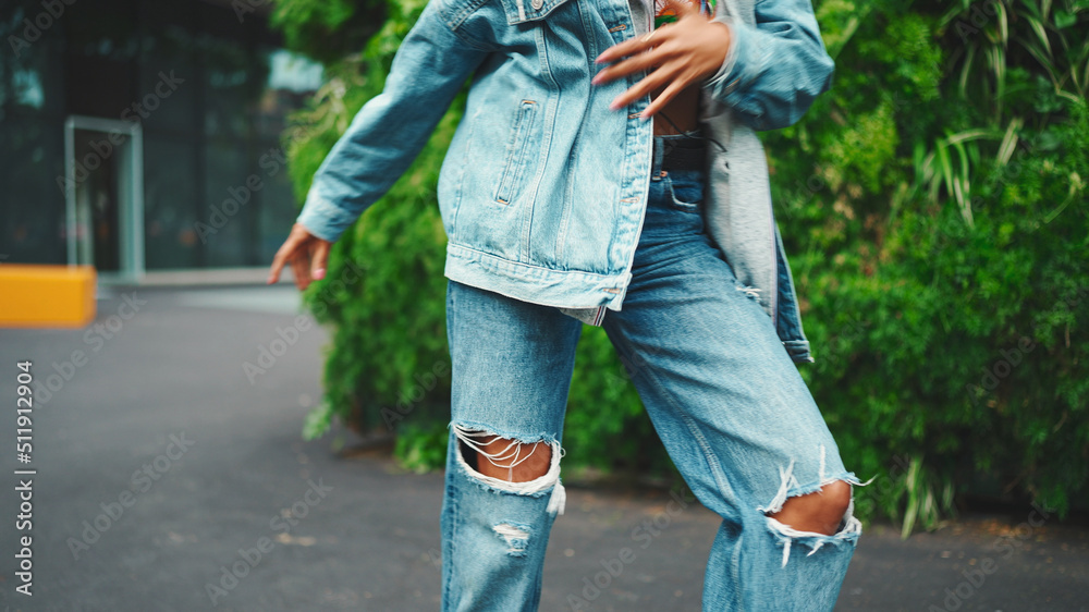 Closeup, smiling African girl wearing denim jacket, in crop top with national pattern walks in city park listening to music on headphones and dancing on green trees background. Closeup, smiling African girl wearing denim jacket, in crop top with national pattern walks in city park listening to music on headphones and dancing on green trees background.