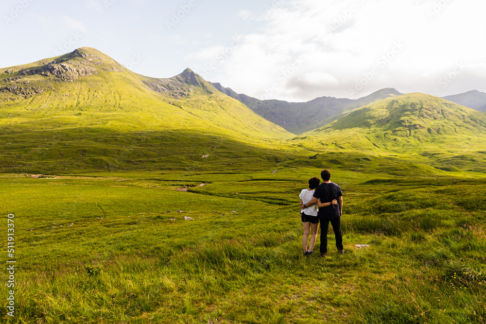 Photo of a couple witnessing a landscape full of mountains on a summer day in the highlands, Scotland