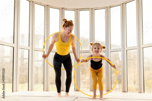 Young fit mom and her daughter having fun with hula hoop in a gym photo