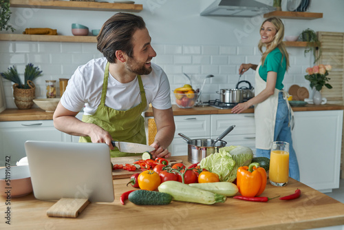 Young man using digital tablet while cooking together with his girlfriend at the kitchen