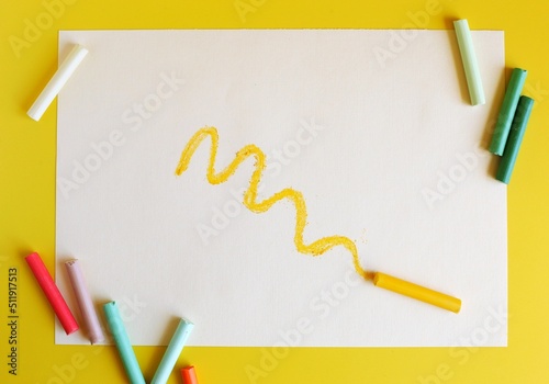 The curved line is drawn in yellow pastel chalk on a white sheet. Soft pastel and a sheet of paper on a yellow background. Top view