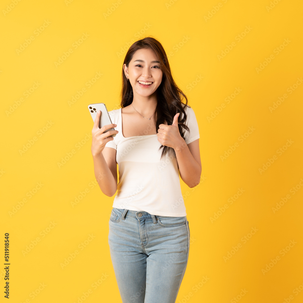 Smiling asian woman white shirt on yellow background use smartphone with thumbs up happy feeling show appreciation Smiling asian woman white shirt on yellow background use smartphone with thumbs up happy feeling show appreciation