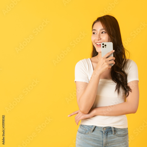 Smiling asian woman white shirt on yellow background using smartphone
