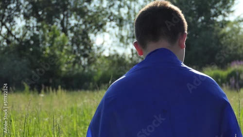 Sad boy looking at the camera with the national flag of Ukraine outdoors in a green field. Ukraine freedom, patriot symbol, victory in war.