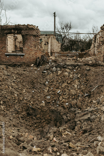 A funnel from a missile shell near a destroyed house in Ukraine