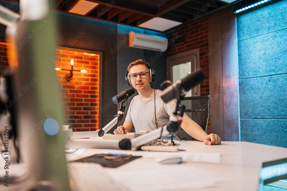 The DJ hosts the program and communicates with the audience on air at the radio station. The announcer reads the news. A male radio host speaks into a microphone and records a podcast The DJ hosts the program and communicates with the audience on air at the radio station. The announcer reads the news. A male radio host speaks into a microphone and records a podcast