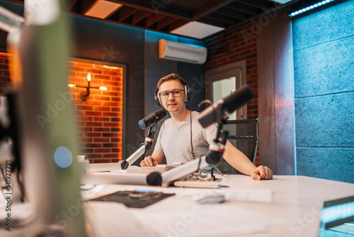 The DJ hosts the program and communicates with the audience on air at the radio station. The announcer reads the news. A male radio host speaks into a microphone and records a podcast photo