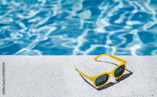 back view of yellow glasses on the white border of a swimming pool with bluish water in the background. concept of vacation and summer.