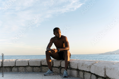 African american man looking away while sitting near the sea and enjoying of the views