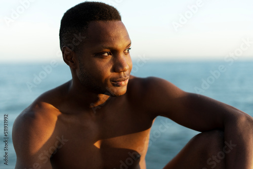 Portrait of smiling young african american man sitting on the beach and looking away