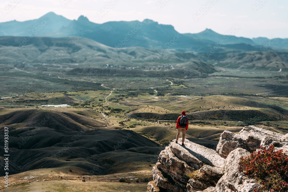 A traveler with a backpack in the mountains. Hiking in the mountains. A journey through the picturesque places of Russia. A man with a backpack on the background of mountains, rear view. Hiking trips