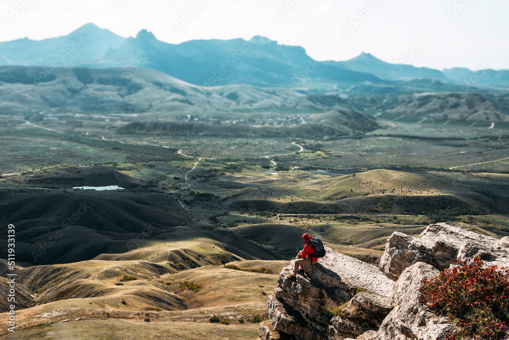 A male tourist is resting after a hard climb up the mountain, panorama. A traveler among the Rocky Mountains. A man is a traveler with a backpack among the rocks. Backpacking in the mountains