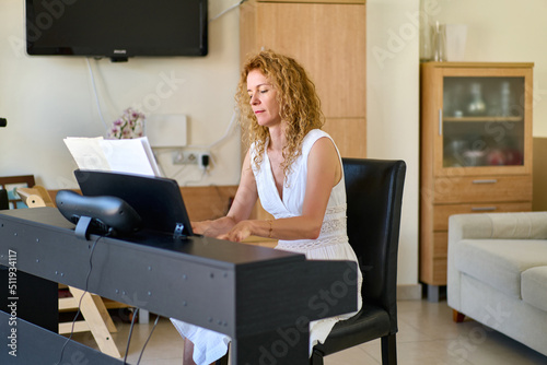 Woman in white dress sitting at the piano. Woman playing piano were digitally modified. Practice at home.