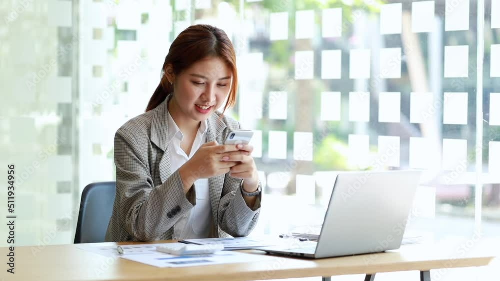 Beautiful Asian woman playing mobile phone in her break from work, she is a marketing manager of a startup company, female leader, supervisor, ceo. Female Leadership Concept. 4K. Beautiful Asian woman playing mobile phone in her break from work, she is a marketing manager of a startup company, female leader, supervisor, ceo. Female Leadership Concept. 4K.