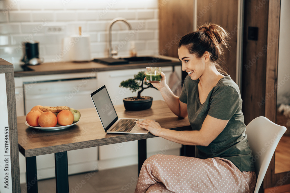 Woman Surfing The Net While Enjoying Breakfast In Her Kitchen At Home