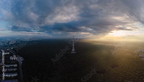 Aerial panoramic sunrise morning city view on telecommunication tower in forest near residential district with scenic sun shining in cloudy sky. Kharkiv  Ukraine