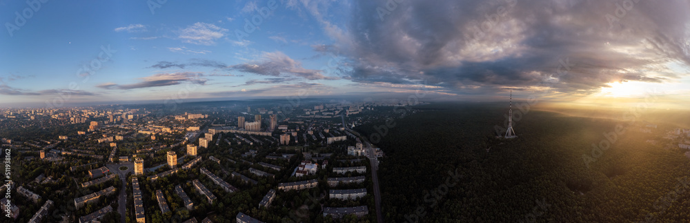 Epic sunrise sun in clouds above green forest, wide panorama view in city residential district. Aerial Pavlovo Pole, Kharkiv, Ukraine. Morning cloudscape and streets