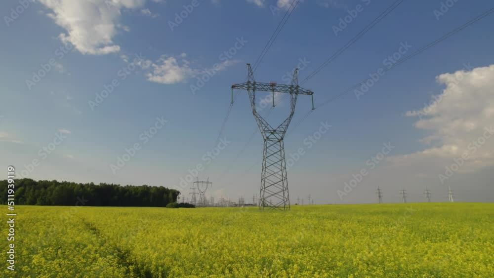 Slow movement of the camera to the high pole of power lines. Pillars of power lines in a beautiful flowering field on a sunny summer day. High quality 4k footage Slow movement of the camera to the high pole of power lines. Pillars of power lines in a beautiful flowering field on a sunny summer day. High quality 4k footage