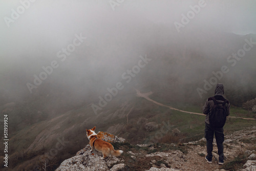 A man and a Pembroke Welsh Corgi climb above the clouds high in the mountains.