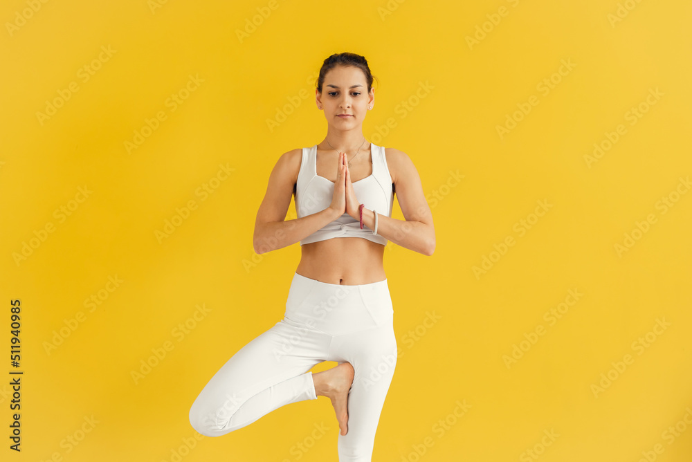 Woman meditating in yoga pose on yellow background