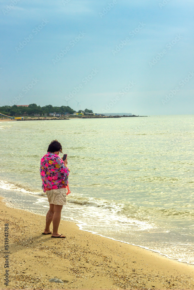 a woman takes picture on the sea beach with smartphone