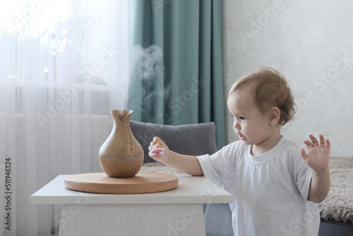 Aromatherapy concept. Little blond-haired European girl at home. Wooden Electric Ultrasonic Diffuser and Essential Oil Aroma Humidifier. Ultrasonic mini aroma diffuser for home.