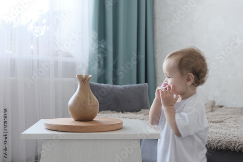 Aromatherapy concept. Little blond-haired European girl at home. Wooden Electric Ultrasonic Diffuser and Essential Oil Aroma Humidifier. Ultrasonic mini aroma diffuser for home.
