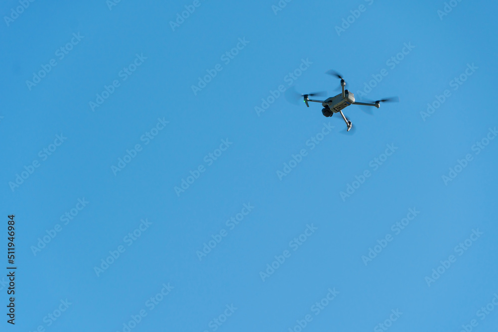 A modern drone against a clear blue sky. The quadcopter hovered motionless in the sky. The use of aircraft for reconnaissance and fire correction. A modern drone against a clear blue sky. The quadcopter hovered motionless in the sky. The use of aircraft for reconnaissance and fire correction.