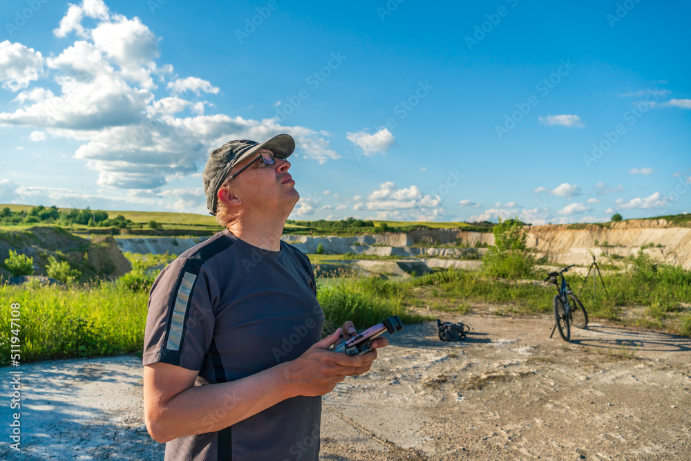 The pilot of an unmanned aerial vehicle holds a drone control panel in his hands. Flying a quadrocopter over an old abandoned quarry. A blogger launches a drone while traveling.
