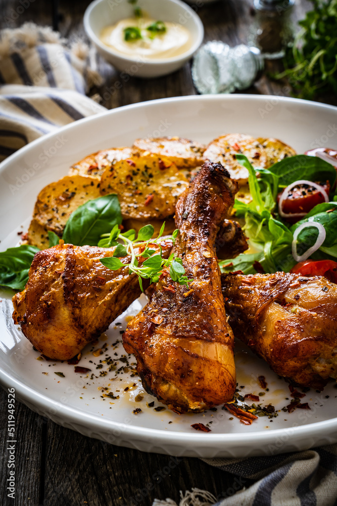 Barbecue chicken drumsticks with fried potato, lettuce and mini tomatoes on wooden table
