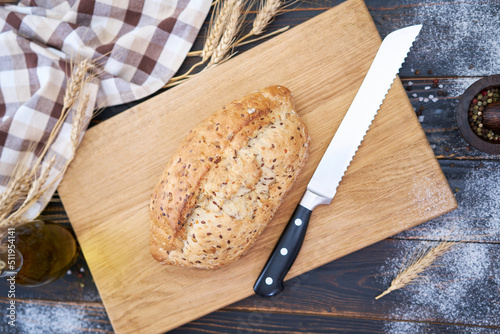 Fresh bread loaf on wooden cutting board at kitchen table photo
