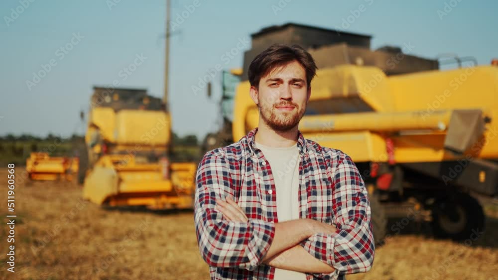 Portrait of proud harvester machine driver with hands crossing on chest. Farmer standing at his combine. Agronomist looking at camera. Rancher at harvesting work on stubble of harvested wheat field. Portrait of proud harvester machine driver with hands crossing on chest. Farmer standing at his combine. Agronomist looking at camera. Rancher at harvesting work on stubble of harvested wheat field.