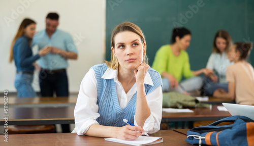Upset girl sitting at table in auditorium during break on background with other students