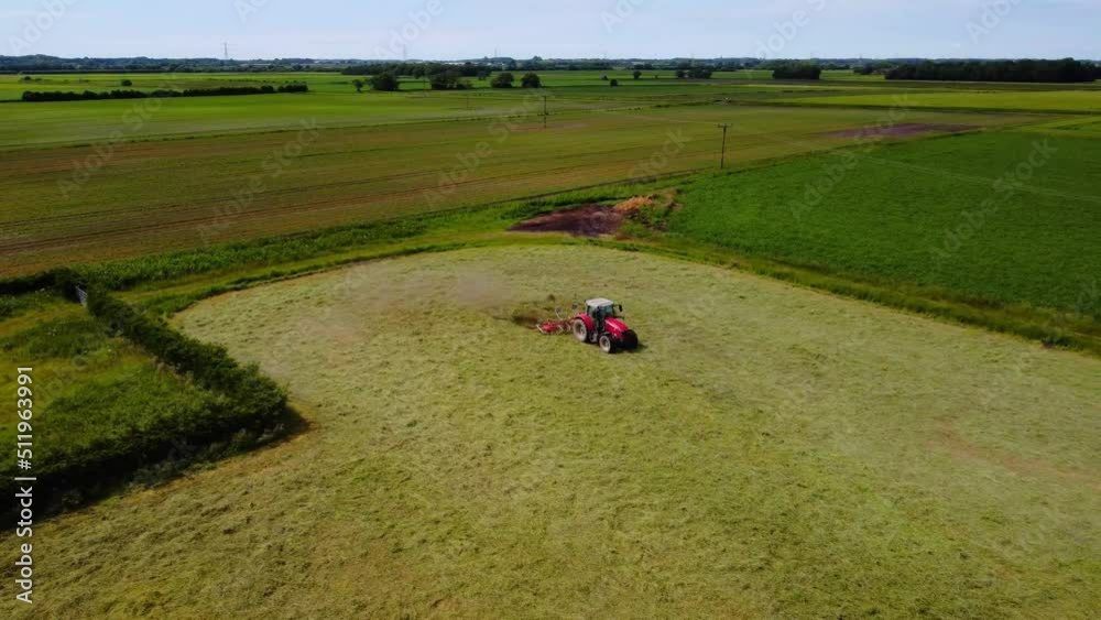 Aerial clip of Tractor and machine turning the cut grass to dry as hay in the English Countryside Aerial clip of Tractor and machine turning the cut grass to dry as hay in the English Countryside