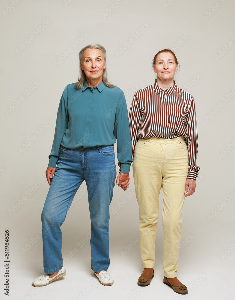 Two happy elderly women friends on grey background. Full length portrait. Two happy elderly women friends on grey background. Full length portrait.