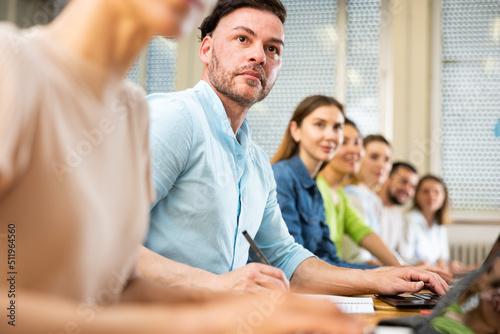 Man university student sitting at table with his group. Students sitting in row.