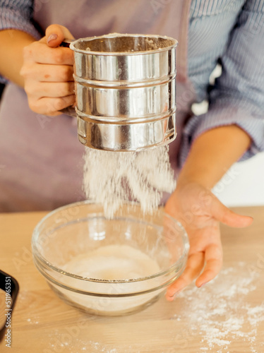 A young woman sifts flour through a sieve, for dough, baking, cake, pie. Modern kitchen.