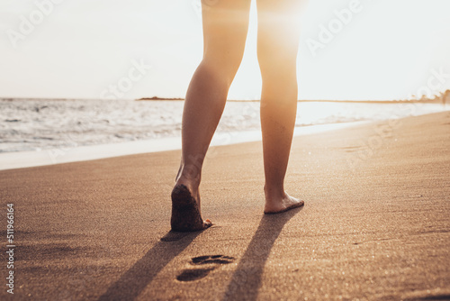 Beach travel - woman walking on sand beach leaving footprints in the sand. Closeup detail of female feet and golden sand on Tenerife beach..