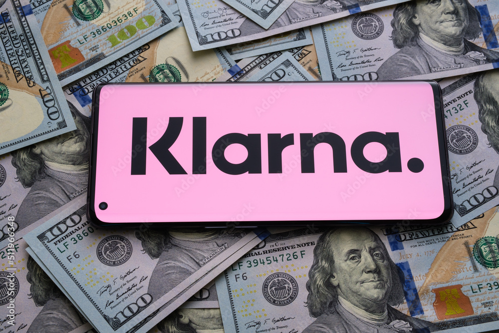 Klarna app logo seen on the screen of smartphone placed on dollar bills