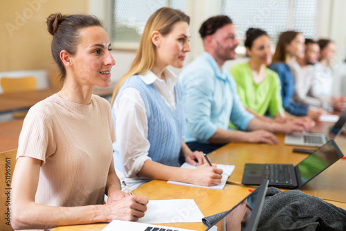 Group of young students searches for information on a laptop and writes it down in a copybooks, studying in a university ..auditorium during classes