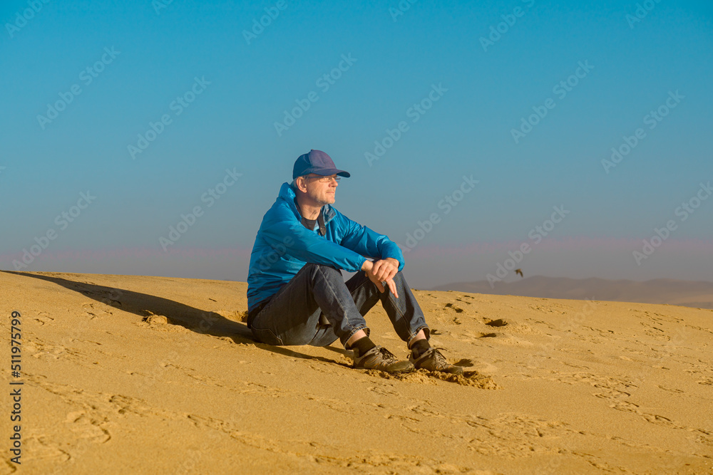 Handsome mature man sitting on the beach by the sea enjoying the view. Sand dunes, and clear blue sky background Handsome mature man sitting on the beach by the sea enjoying the view. Sand dunes, and clear blue sky background