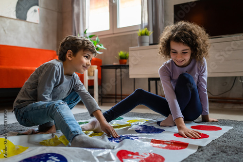 Brother and sister siblings small caucasian boy and girl child play twister game on the floor at home alone real people family growing up leisure concept copy space photo