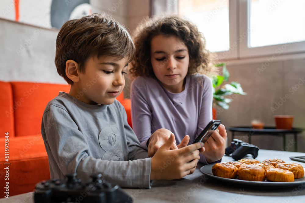 Siblings brother and sister boy and girl or children friends using mobile phone smartphone at home in room to watch video make a call or play online games leisure family concept real people copy space