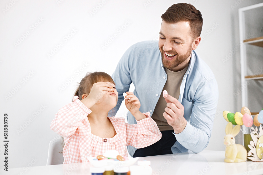 Girl with Down syndrome and her father playing with Easter colored eggs Girl with Down syndrome and her father playing with Easter colored eggs