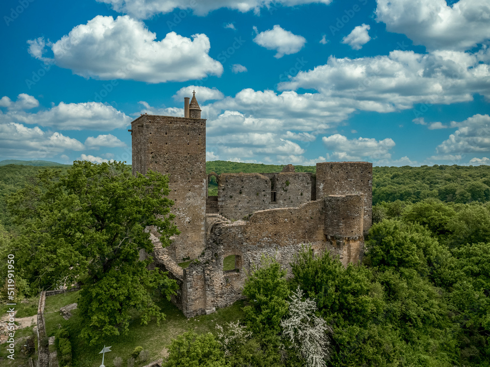 Close up aerial view of the rectangular keep, ruined Gothic palace and circular defensive tower at Brancion castle and medieval village in Central France with cloudy blue sky