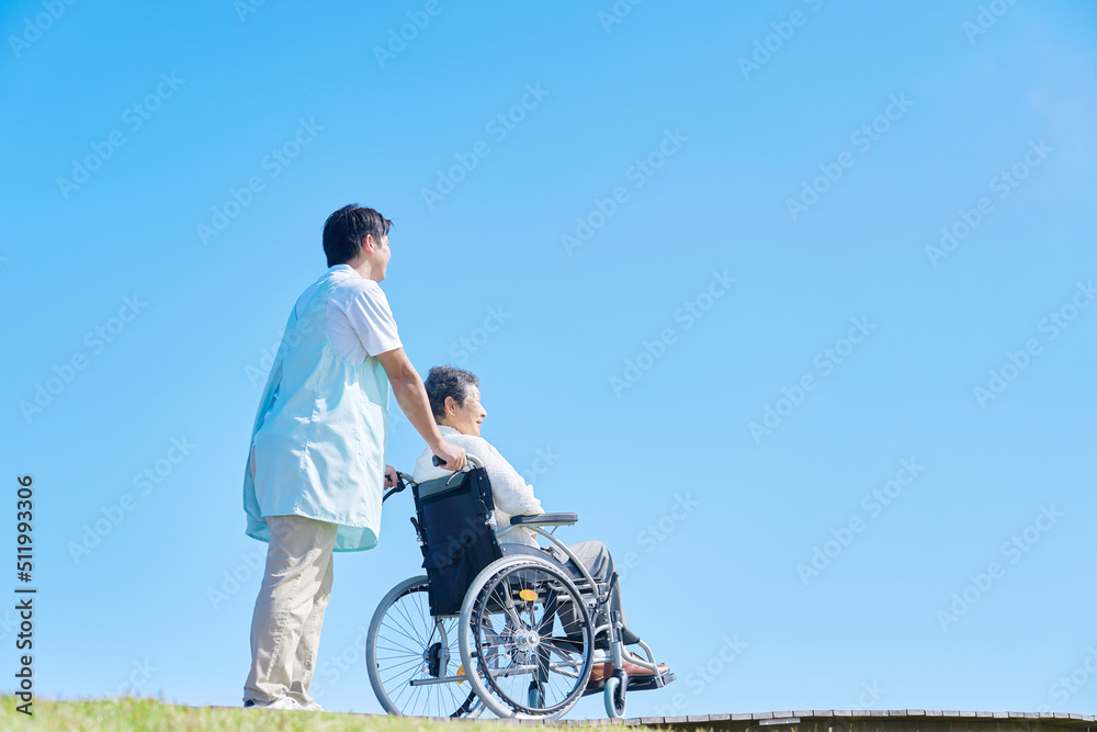 Obraz premium 看護師と屋外を車椅子に乗って散歩する高齢者女性